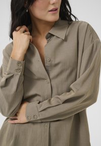 Light brown button-up shirt featuring a classic collar, long sleeves with button cuffs, smooth texture, and subtle sheen.