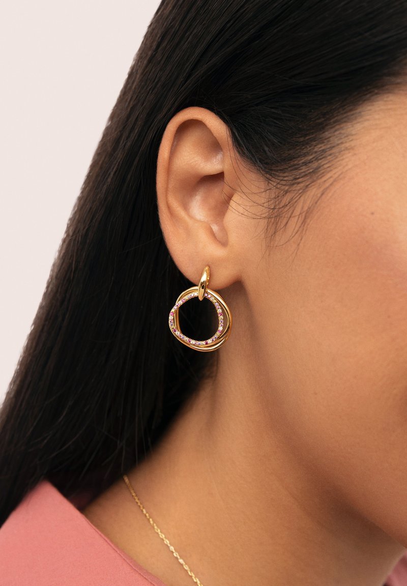 Orecchini a cerchio dorati con forme circolari intrecciate, accentuati da gemme rosa lungo il bordo interno.