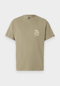 Olive green cotton t-shirt with a round neckline. Front features a circular white graphic text design stating "FREEDOM FROM CHAOS." Short sleeves.