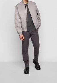 Giubbotto bomber grigio chiaro con texture liscia, maglietta in maglia grigio scuro, pantaloni grigio scuro e stivali alla caviglia neri con suole robuste.