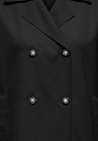 Manteau noir croisé à larges revers avec quatre grands boutons foncés, montrant la partie supérieure du torse avant et les poches.