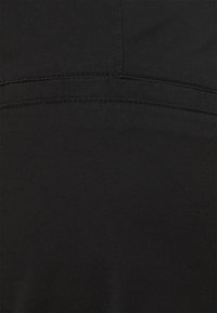 Primo piano di un tessuto nero, che mostra una superficie liscia con un delicato motivo a trama diagonale e cuciture rinforzate lungo le giunture.