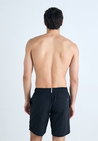 Shorts de bain noirs avec une taille élastique, dotés d'une seule poche arrière et d'un détail de cordon de serrage contrastant à l'arrière.