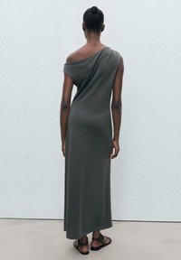 Sleeveless, off-shoulder dress in a soft, dark olive green fabric, featuring a long, flowing silhouette and a relaxed fit.