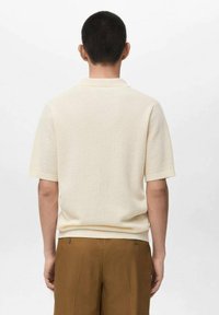 Polo de manga corta y textura en beige claro, con cuello clásico y diseño ajustado, combinado con pantalones marrones.