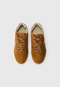 Een paar bruine suède sneakers met gemusterde veters en leren accenten, gezien vanaf boven op een effen witte achtergrond.