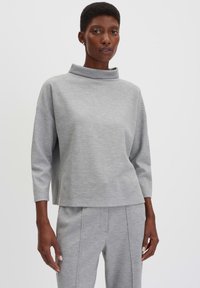 Grijze, lange mouwen pullover met een hoge hals, gemaakt van textuurstof. Heeft een losse pasvorm en afgezakte schouders, gedragen met bijpassende broeken.