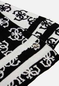Sciarpa lavorata a maglia con strisce alternate in bianco e nero, abbellita da un motivo con logo in evidenza e un piccolo spillo argentato.