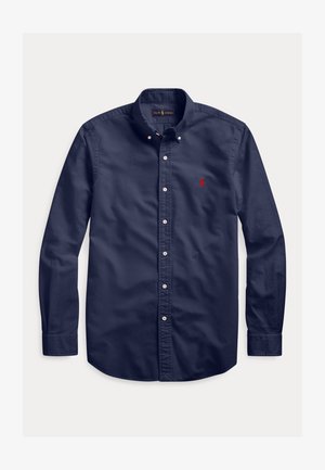 Laivastonsininen pitkähihainen napillinen kauluksellinen paita, jossa pieni punainen kirjailtu logo vasemmalla rinnassa.