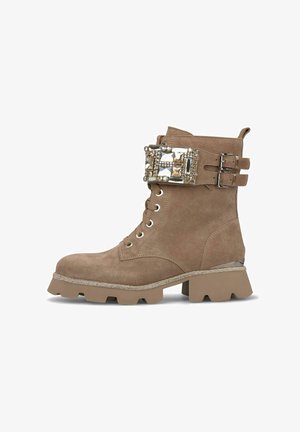 Stivaletti in suede marrone con tacco spesso, decorati con una fibbia metallica e due cinturini, dotati di una suola texture.
