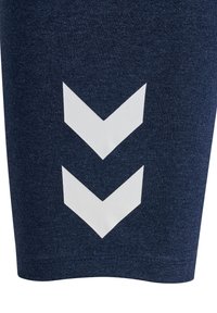 Zbliżenie ciemnoniebieskiej tkaniny z dwoma dużymi białymi strzałkami szewronowymi skierowanymi w dół, nadrukowanymi pionowo.