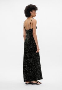 Čierna maxi šaty s kvetinovým potlačou z zamatového materiálu, s tenkými ramienkami, priliehavým strihom a nízkym chrbtom. Doplnené o strappy čierne sandále.