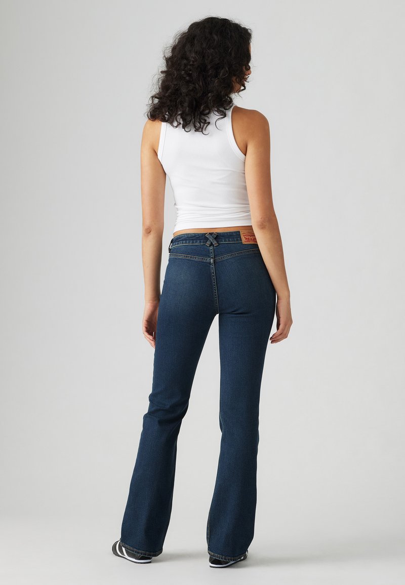 Dunkelblaue, ausgestellte Jeans mit einem klassischen Fünf-Taschen-Design, kontrastierenden Nähten und einem braunen Lederpatch hinten.