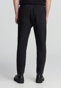 Czarne dżinsy w prostym kroju, z pięcioma kieszeniami, tylnym logo i przeszyciami. Noszone z czarnymi butami.