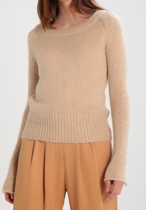 Maglione beige lavorato a maglia con scollo a barca, orlo e polsini a coste, caratterizzato da una texture morbida e pelosa e una vestibilità rilassata. Abbinato a pantaloni marrone chiaro.