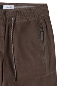 Bruine broek van zacht materiaal met een elastische tailleband. Voorzien van een trekkoord en een ritszak aan de zijkant.