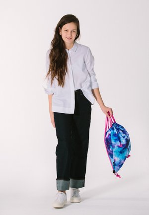 White button-up shirt, dark denim jeans with cuffed hems, white sneakers, and a blue tie-dye drawstring bag with pink accents.