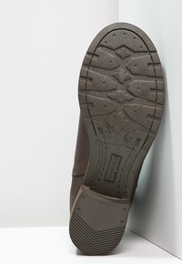 Suola di scarpa in pelle marrone con una superficie strutturata e patternizzata e battistrada pronunciato per una presa salda. Presenta una leggera curvatura e cuciture laterali.
