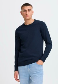 Dunkelblauer Rundhals-Pullover aus Strickstoff, mit langen Ärmeln und gerippten Bündchen und Saum, kombiniert mit hellblauen Jeans.