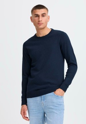 Navy blue crewneck sweater made of knitted fabric, featuring long sleeves and ribbed cuffs and hem, paired with light blue jeans.