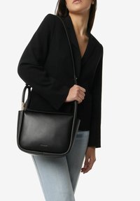 Czarna skórzana torebka o eleganckim, minimalistycznym designie, z gładką fakturą, pojedynczym regulowanym paskiem i złotymi akcentami.