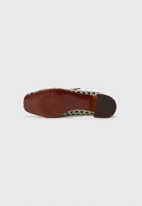 Flat shoe with a black and white geometric pattern, rounded toe, and a brown rubber sole. Minimalist design with a smooth texture.