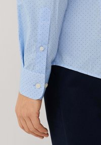 Lichtblauwe shirt met kleine donkerblauwe stippen, met een knoopmanchet en een puntige mouwontwerp, gemaakt van soepel stof.