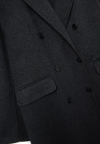 Cappotto giacca doppiopetto in lana grigia scura con finitura testurizzata, due tasche anteriori e bottoni neri per la chiusura.