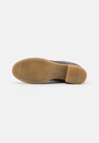Semelle de chaussure avec une base en caoutchouc brun texturé et des rainures prononcées. La tige est en suède gris doux, formant une forme arrondie.