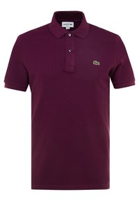 Burgundská polo košile vyrobená z texturované látky, se zapínáním na dva knoflíky a malým zeleným vyšitým logem na hrudi. Krátké rukávy.