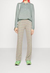 Pull vert avec col et boutons, associé à un pantalon rayé rose, jaune et beige. Comprend des baskets vertes avec semelle noire.