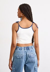 White cropped tank top with navy straps and bow details; paired with light blue denim cargo pants featuring patch pockets and elastic waistband.
