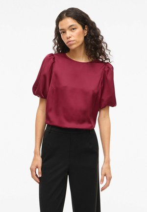 Blouse en satin bordeaux avec manches courtes bouffantes, encolure ronde et texture lisse, associée à un pantalon noir.