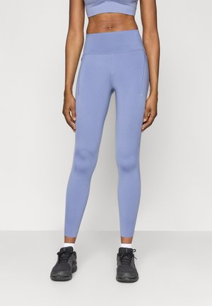 Leggings de tiro alto en azul claro, fabricados con tejido elástico, con una textura suave y bolsillos laterales, combinados con zapatillas deportivas negras.