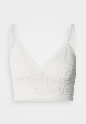 Bralette en dentelle blanche de forme triangulaire, avec un tissu supérieur texturé et une bande élastique côtelée, des bretelles réglables et une finition lisse.