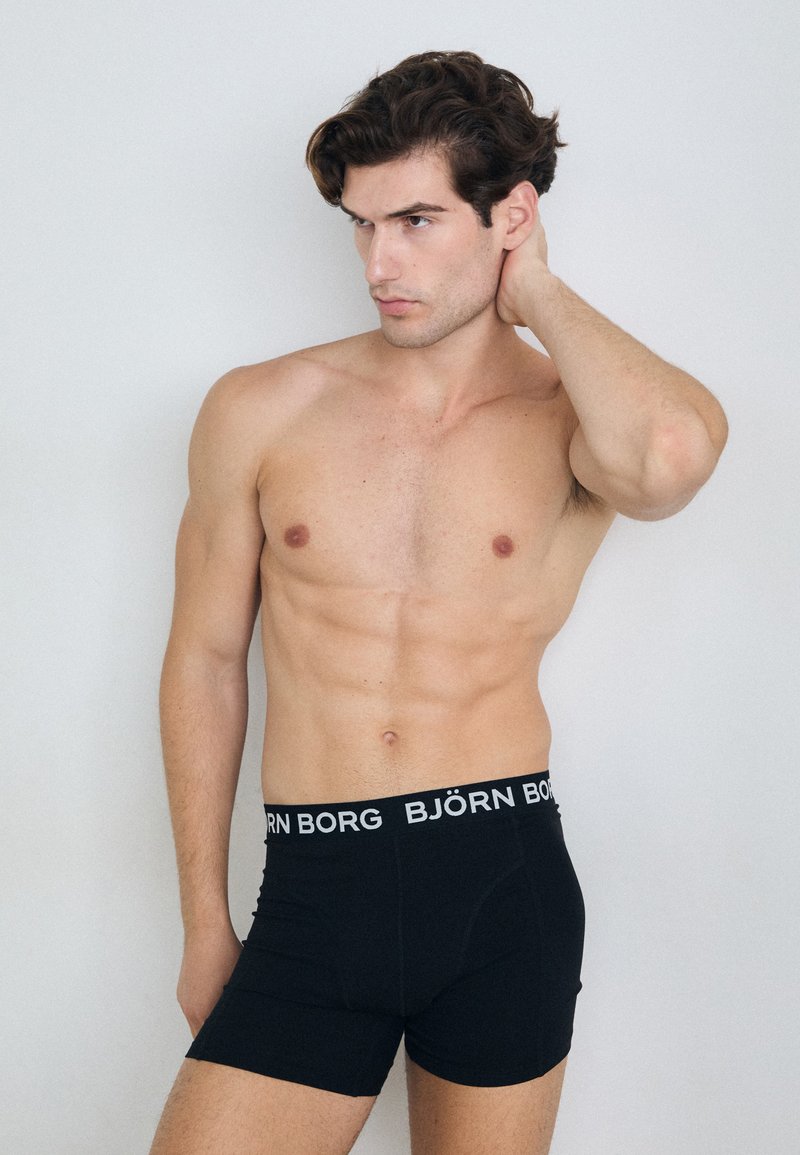 Boxer shorts noirs avec un logo "BJÖRN BORG" blanc sur la ceinture. Le tissu semble lisse et extensible, s'ajustant parfaitement autour de la taille.