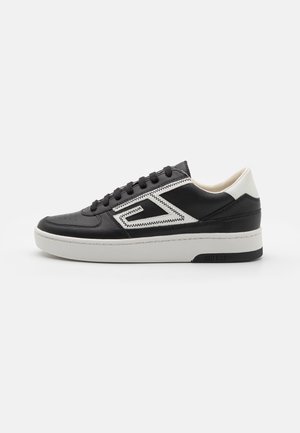 Baskets basse noir et blanc avec un détail de couture en zigzag, lacets noirs, semelle blanche et logo "GUESS" sur le côté du talon.