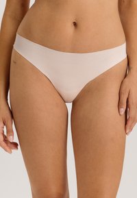 Lichtroze katoenen string met een zachte textuur, voorzien van een naadloze tailleband en een minimalistisch ontwerp voor comfort en flexibiliteit.