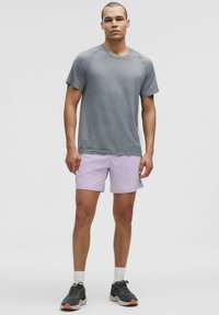 Chemise courte à manches gris texturé, shorts violet clair, chaussettes de sport blanches et baskets noires avec semelles brunes. Design athlétique simple.