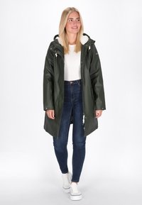 Zaļš ūdensnecaurlaidīgs parkas ar polāru oderi kapuces iekšpusē, ar rāvējslēdzēju un pogām. Kombinēts ar zilajiem šaurajiem džinsiem un baltiem sporta apaviem.