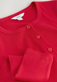 Rode geribde langemouwen shirt met ronde halslijn en drie bijpassende rode knopen langs de voorkant.