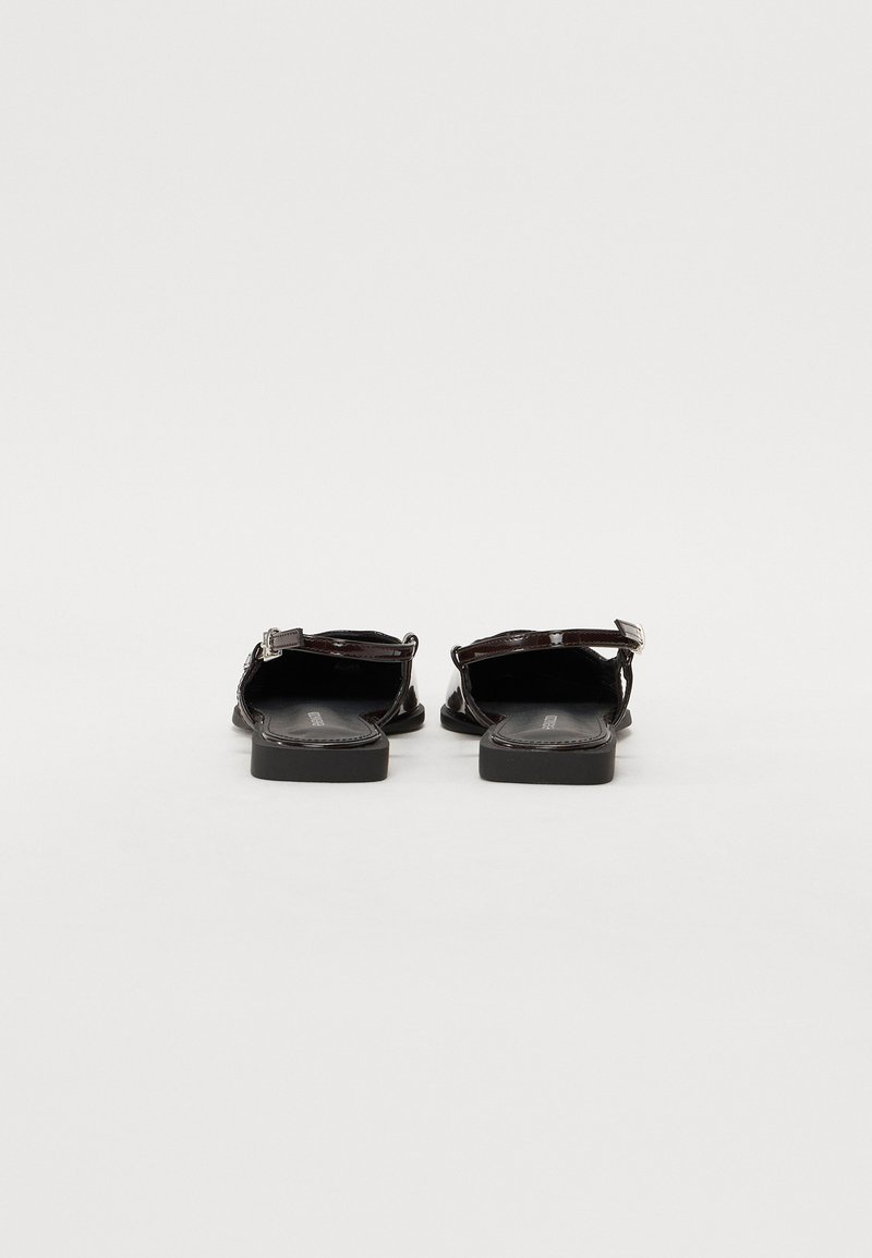 Sandales en cuir verni noir avec une semelle plate, une bride de cheville et un dos ouvert. Présente un design simple et un détail de surpiqûre contrastant.