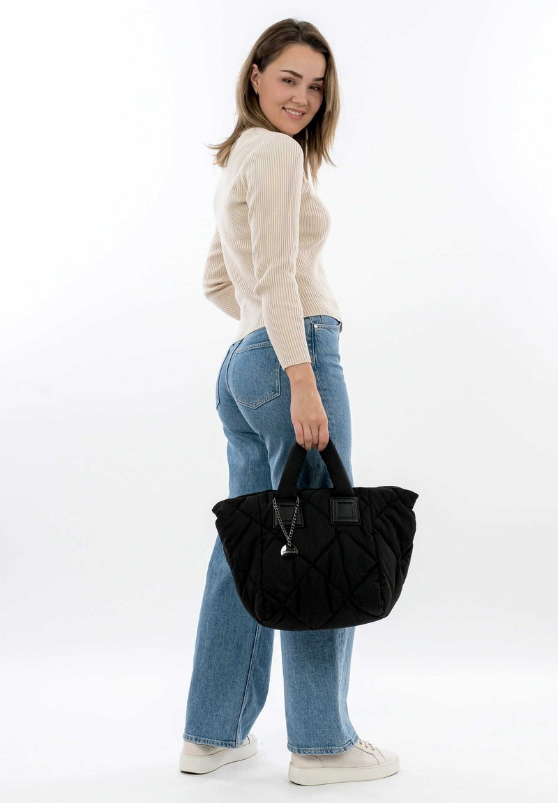 Black quilted tote bag with dual handles and a charm pendant. Soft fabric, rounded shape, prominent stitching pattern, and structured base.