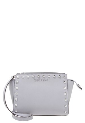 Hellgraue Michael Kors Crossbody-Tasche mit silbernen quadratischen Nieten entlang der Kanten und verstellbarem Riemen.