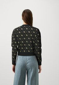 Black knitted sweater with a diamond pattern and gold accents, ribbed cuffs, and hem. Worn with light blue wide-leg trousers.