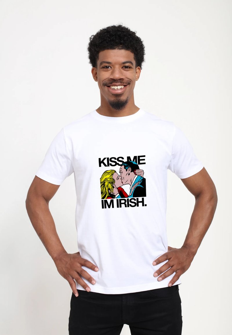 Bílá tričko s grafickým designem páru, který se líbá, a nápisem "KISS ME I'M IRISH" tučným černým písmem v barevném karikaturním stylu.