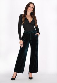 Černý bodysuit s dlouhým rukávem a výstřihem do V, spárovaný s tyrkysovými sametovými kalhotami s širokým střihem, které mají elastický pas a šňůrku na stažení.