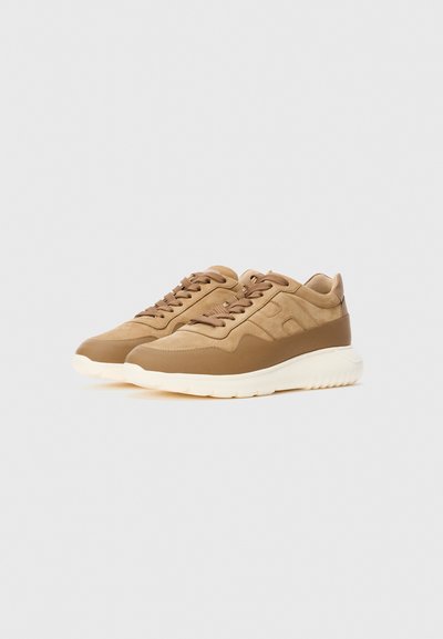 Un paio di sneakers in pelle scamosciata e pelle marrone con suole bianche spesse e lacci marroni su uno sfondo bianco.