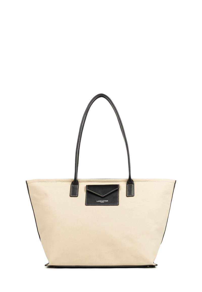 Borsa tote in tela beige con dettagli in pelle nera, base piatta e manici lunghi. Presenta una tasca nera con dettagli di cucitura sul davanti.