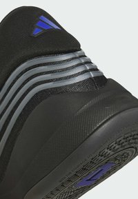Chaussure de sport noire avec une tige en tissu, des accents rayés gris, une semelle texturée et un détail de logo bleu près du talon.